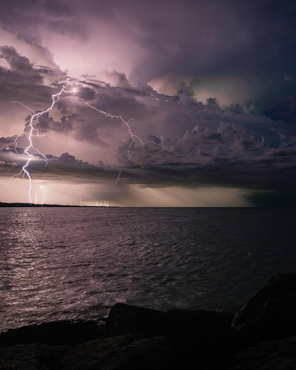 Lightning strikes over Lake Michigan in Muskegon at night, with dramatic clouds illuminated in the sky.
