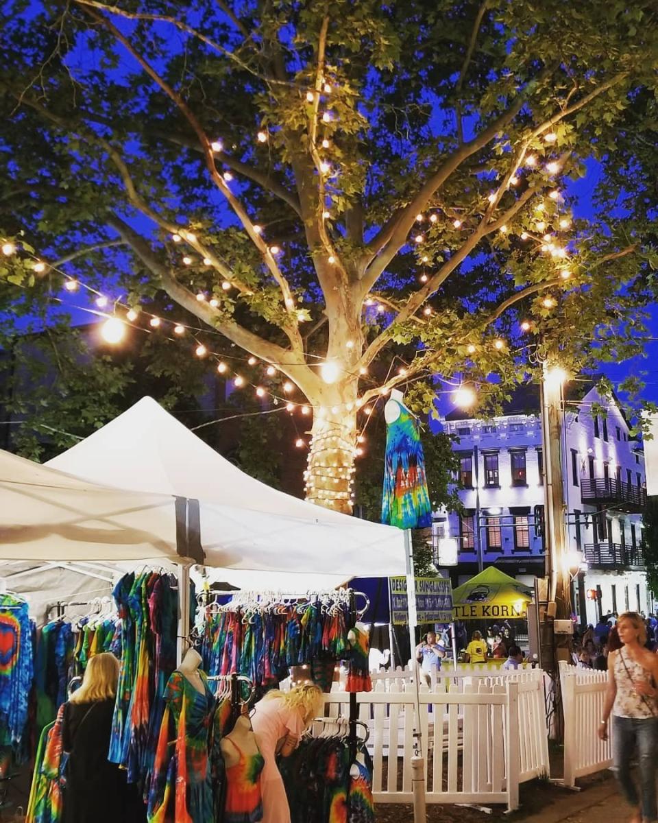 A tree strung with white lights shining down on colorful booths at a street festival in Mainstrasse Village