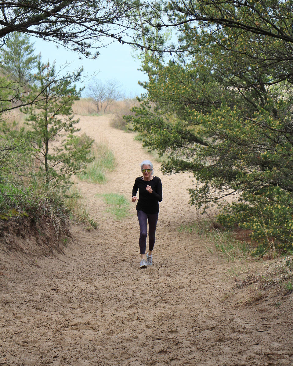 A woman hikes down a dune trail. Pine trees surround her.