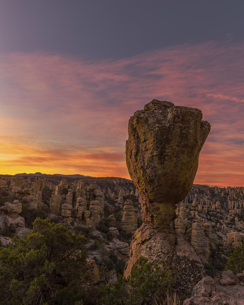 Large oblong rock formation standing tall above a field of similar odd-shaped rock formations at sunset