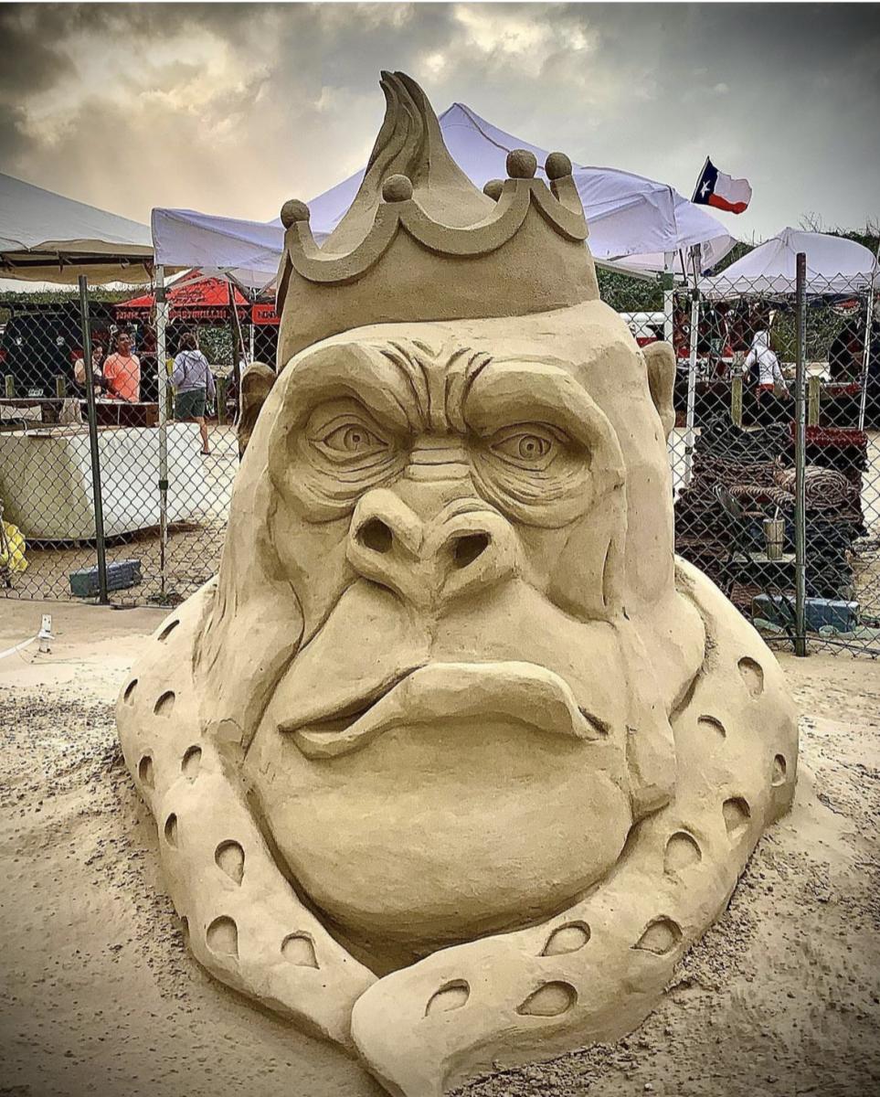 Sand sculpture of an angry-looking gorilla with a crown on top of his head and a regal collar.