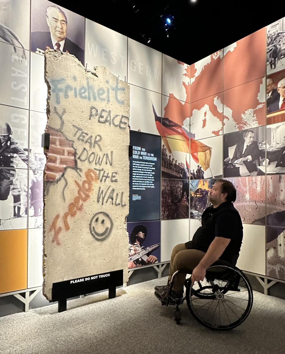 Wheelchair user looking up at large piece of Berlin Wall fragment on display at National Museum of U.S. Army in Fairfax County VA