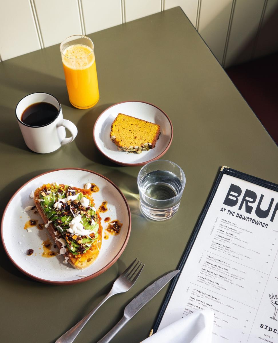 A spread of avocado toast, a slice of bread, orange juice, coffee and water.