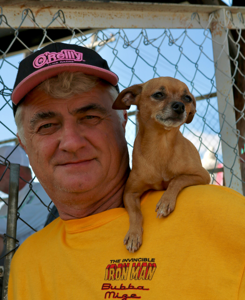 A man posing for the camera with his small dog perched on his sholder.
