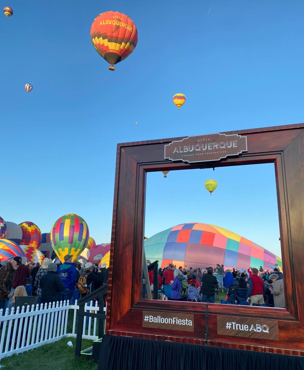 The Visit Albuquerque frame frames a balloon inflating in the background with the Visit Albuquerque balloon floating overhead