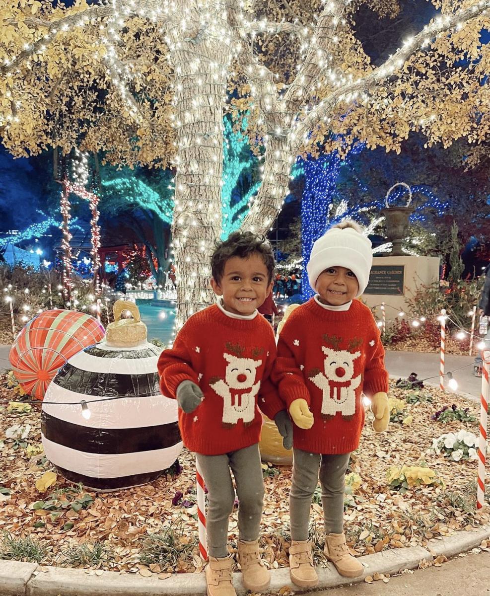 A pair of boy twins in matching outfits surrounded by christmas lights