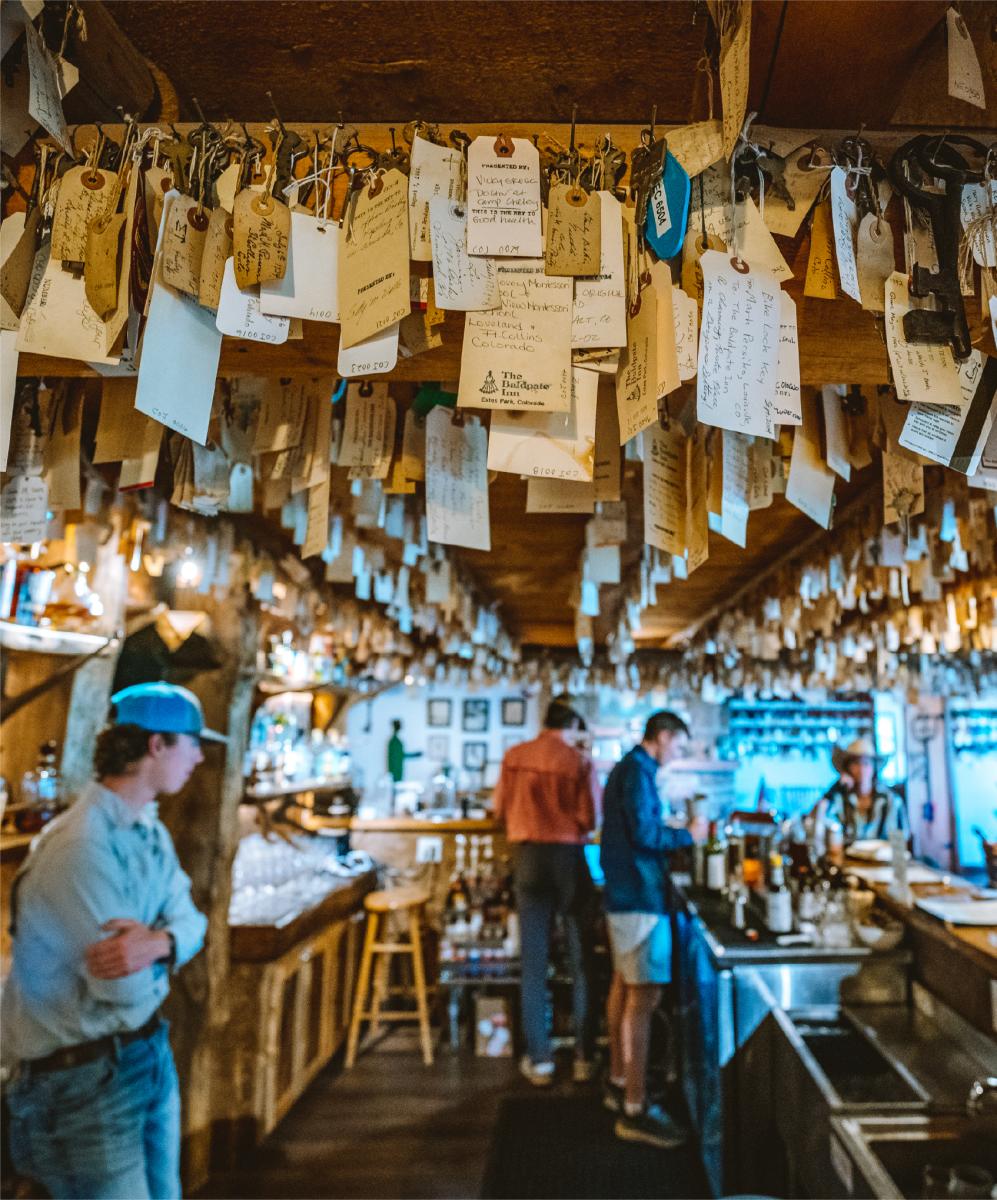 This is an image of Seven Keys Lodge in Estes Park that shows three people behind the bar with thousands of keys hanging from the ceiling of the establishment.