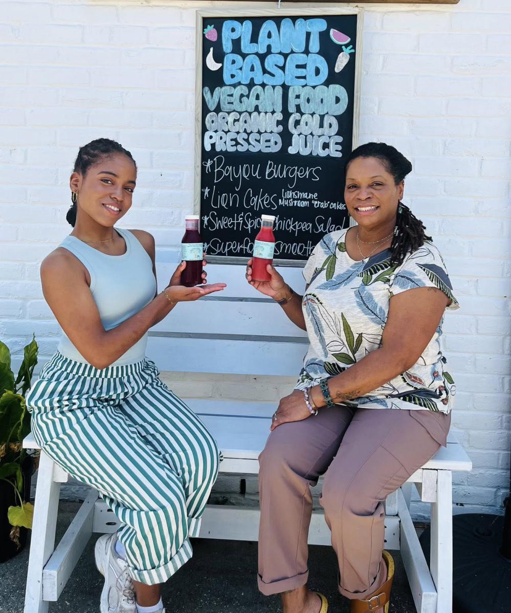 Alicia and Carmen Norman of The Earthly Elephant display their bottled juices, seated outdoors on a bench.