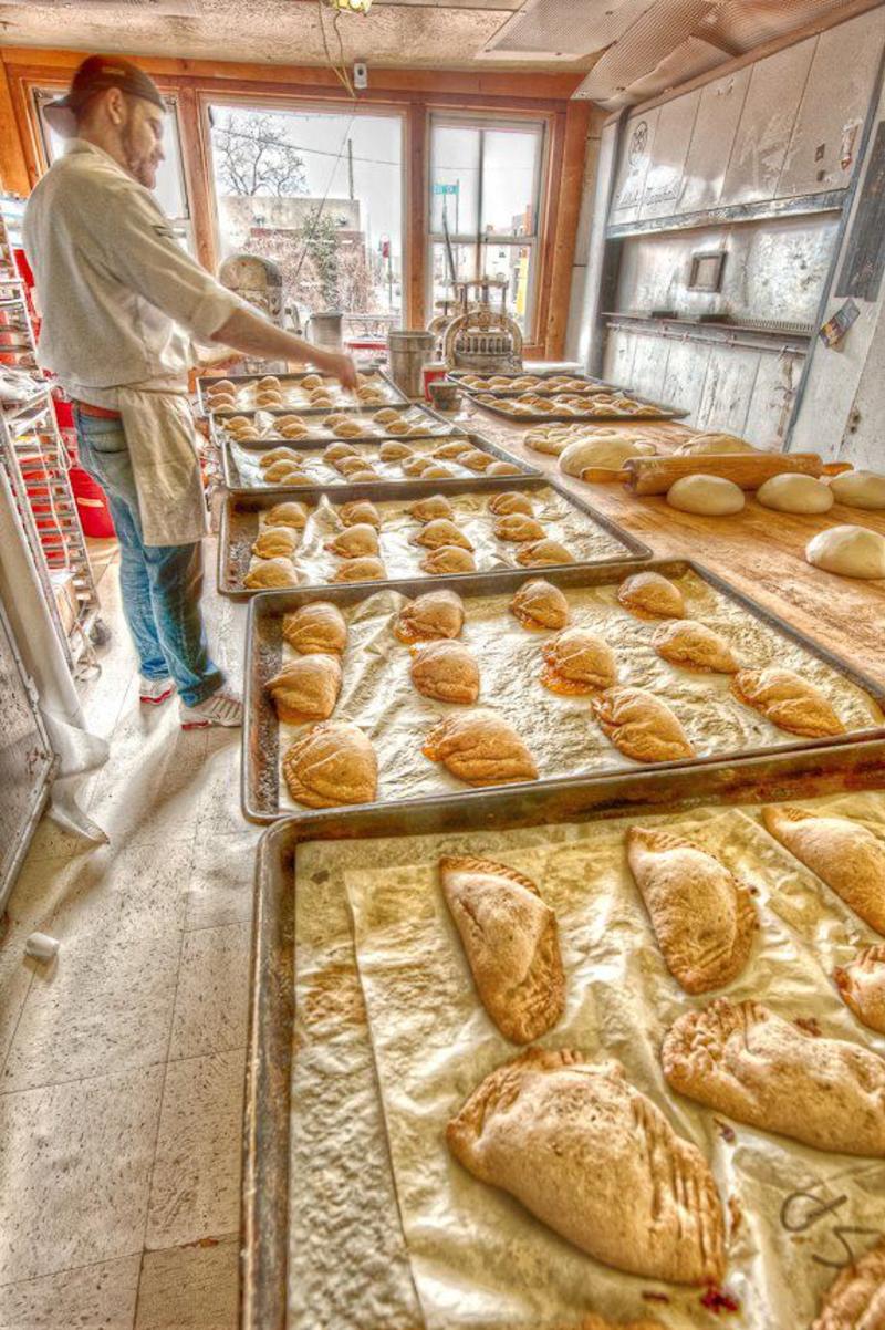 A baker in front of trays of empanadas and rolls at Golden Crown Panaderia