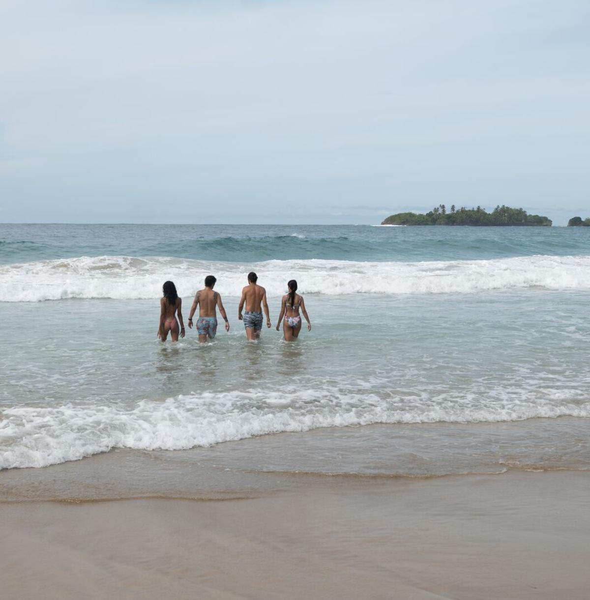 Tourists entering the sea at a beach on Bastimentos Island with a small island in the background.