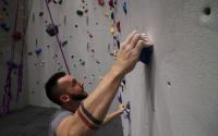 A man looks for his next handle while climbing the wall at Bliss Climbing and Fitness