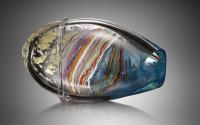 A sculpture that looks like an oval vase turned on its side. It looks like multiple layers of glass, with the innermost layer formed of colorful bands (pink, lavender, red, orange, green, brown, white, blue, and more). The next layer looks clear or blue. The outermost layer appears clear with silver stripes and a golden leopard-like pattern.