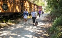 two people walking on rail trail with their dog next to northern central railway of york's steam engine