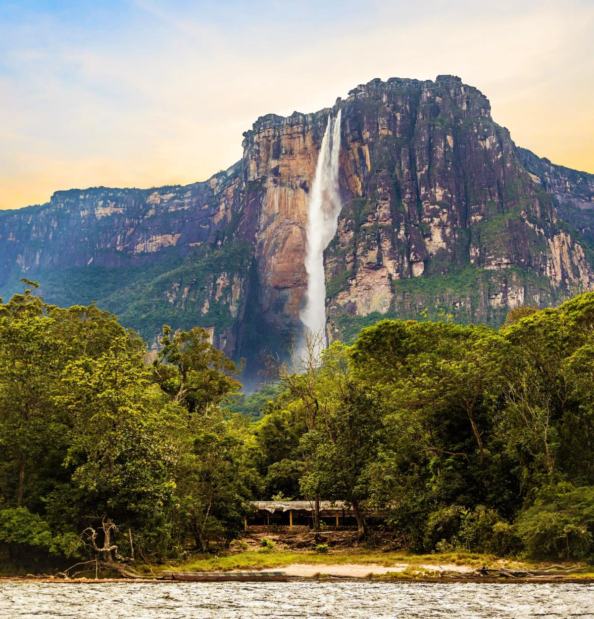 A towering waterfall, known as Angel Falls in Venezuela, plummets from a flat-topped mountain, surrounded by lush, green jungle.