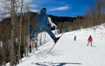 A skier does a Spread Eagle of a small jump on a ski run at Park City Mountain