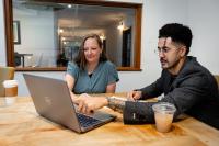 A man points to a laptop showing a woman something on his screen