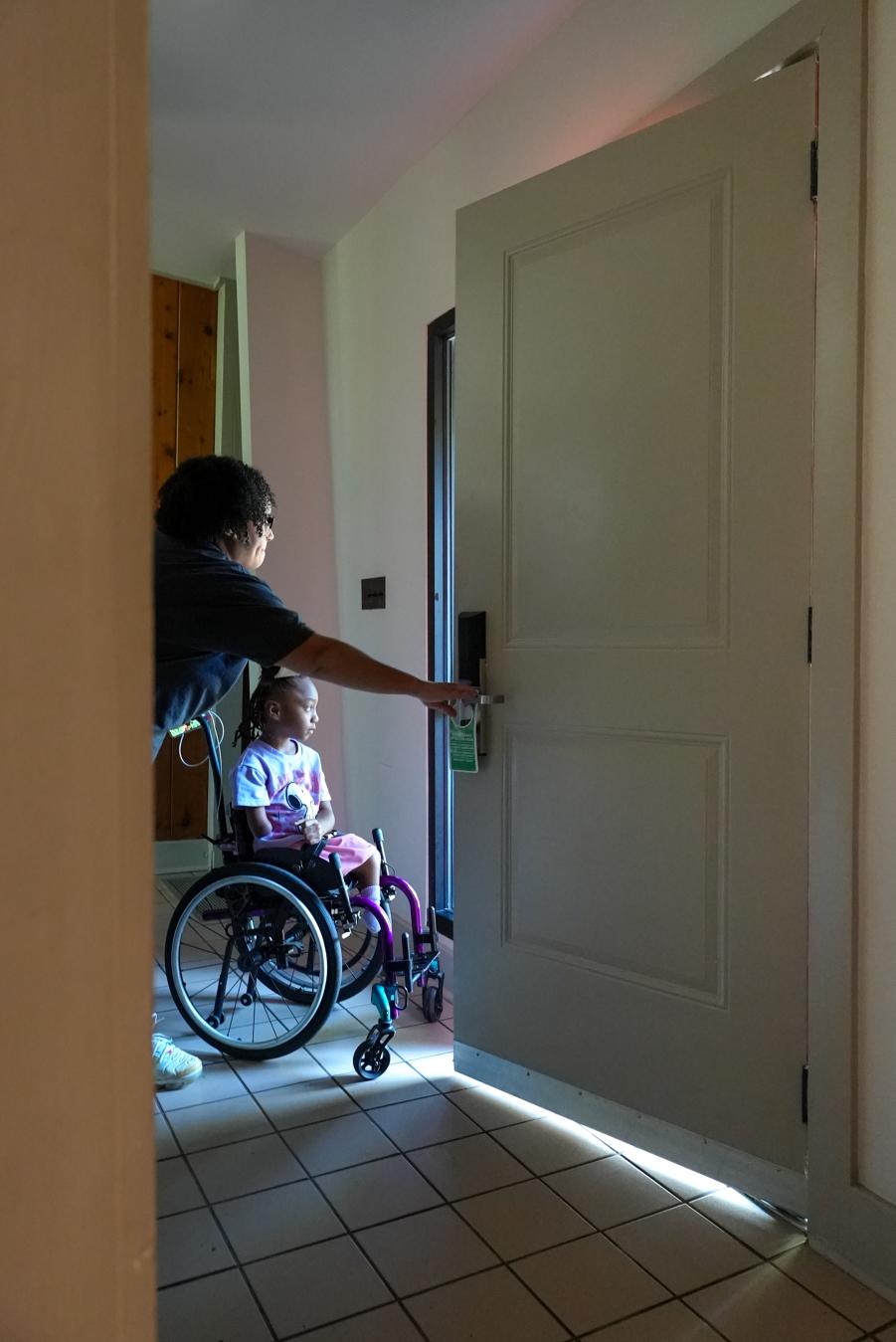 A mother opening an accessible, friendly door for her daughter in a wheelchair.