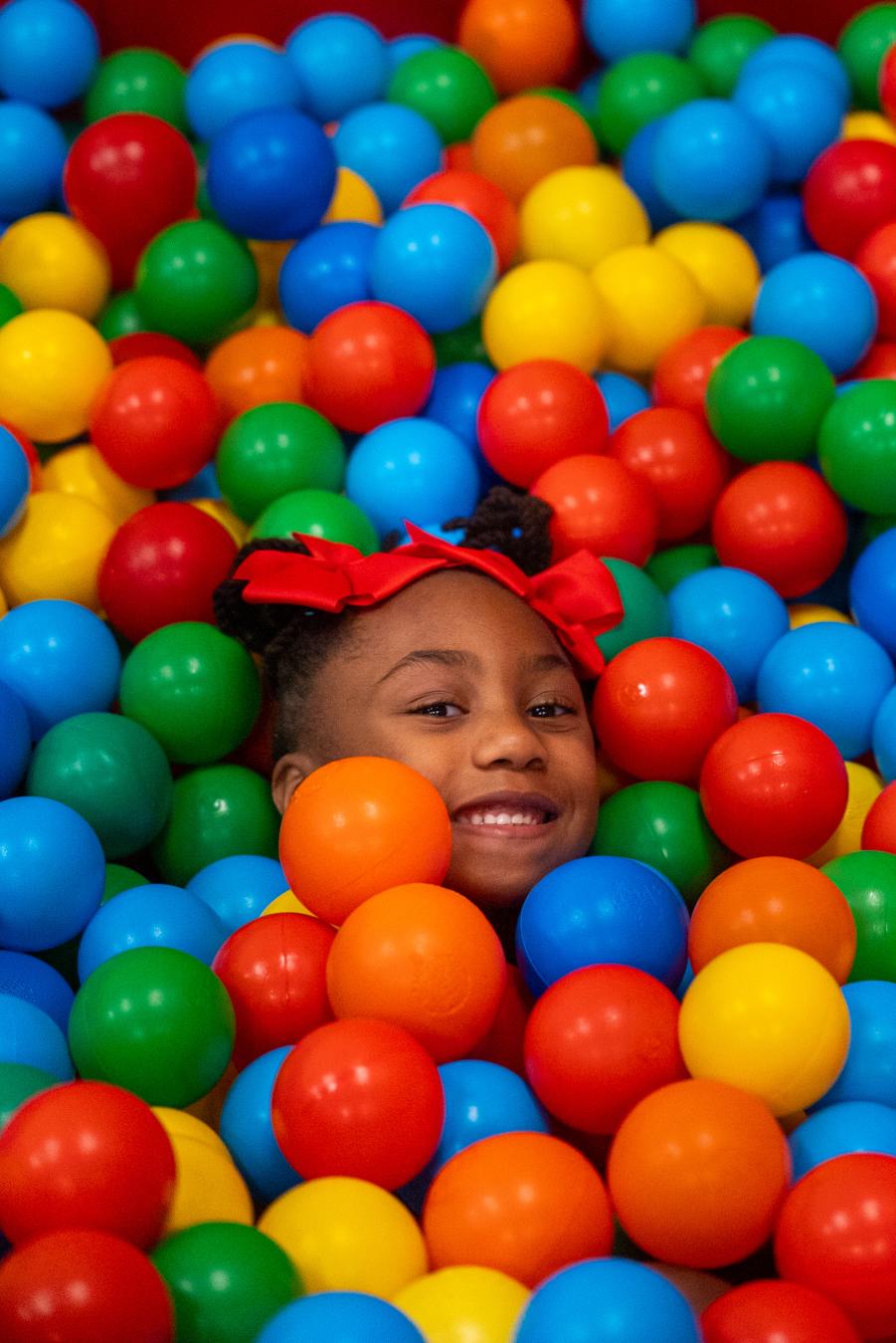 Girl surrounded by colorful balls in the ball pit at the Imagination Place.