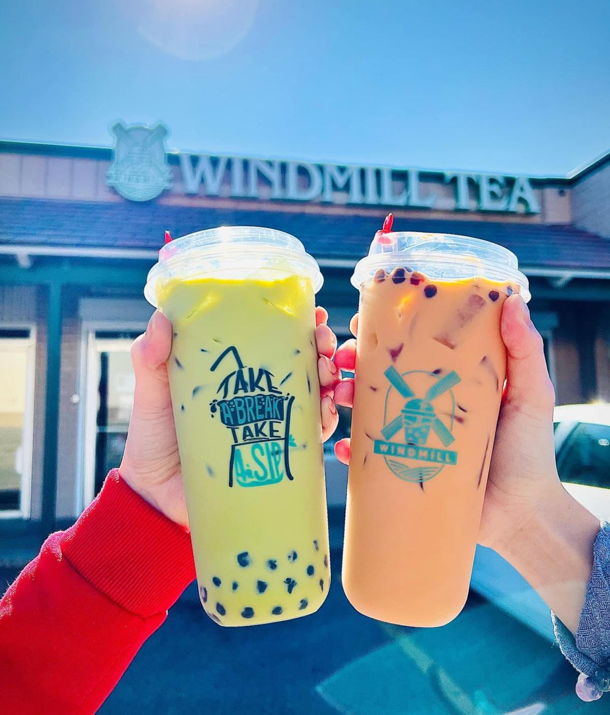 A photo of two people "cheers"ing with milk tea drinks from Windmill Tea.