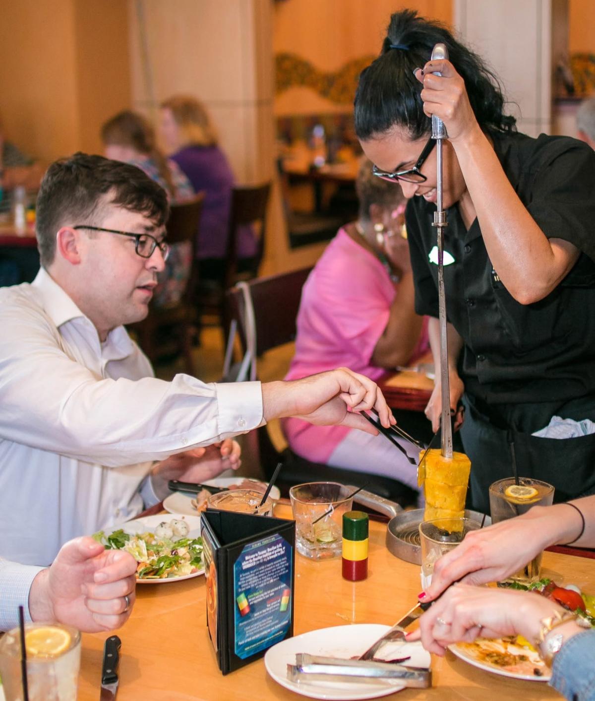 Someone cuts a piece off a grilled pineapple at Tucanos Brazilian Grill.
