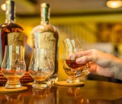 A person holds a small glass of bourbon as part of a bourbon flight at J. Henry and Sons Distillery