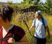 A woman and a man hiking through a grassy section of the Ice Age Trail on a sunny day. The woman is wearing a backpack and the man is carrying a walking stick.