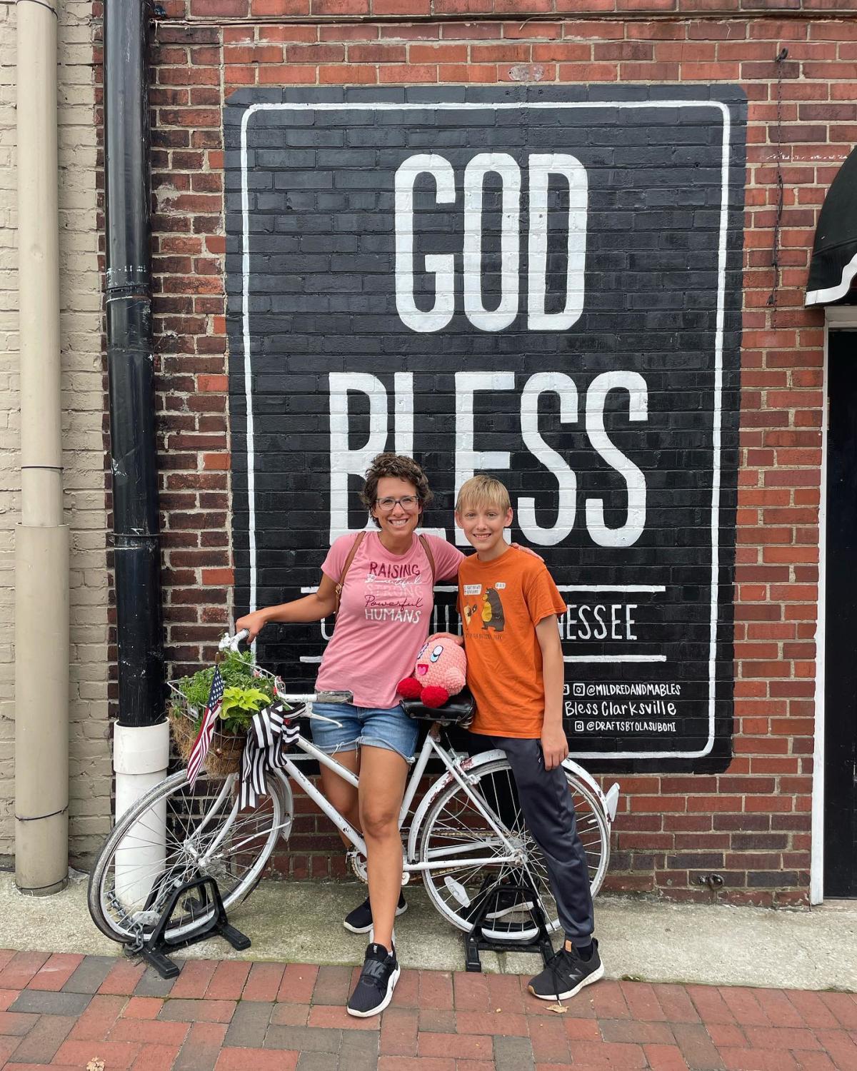 woman and young boy pose on a bicycle in front of a mural