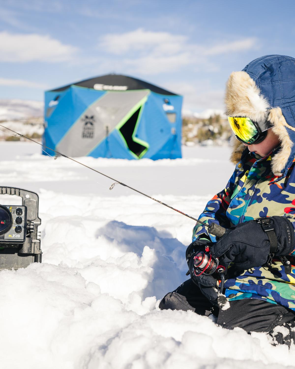 A child sits in the snow on frozen Grand Lake ice fishing.