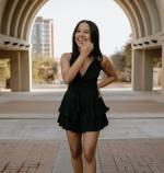 Photo of women in a black dress standing in an archway and smiling towards camera