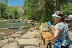lady painting in front of clear creek