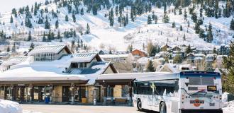 A bus pulls into the Old Town Transit Station in front of snowy ski runs in Park City, UT