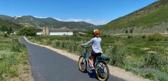 Woman riding an electric bike along a paved path with a white barn in the background