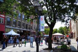 A street festival with tents, people walking through the street and a light pole with a sign reading "Oneonta" in the foreground.