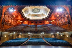 Picture of the Community Arts Center from the stage looking out to the audience. The venue is empty but lit up by lights highlighting the beautiful architecture.