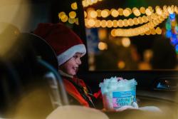 Picture of kid in a car seat holding a bucket of Knoebels cotton candy as the family drives through the Joy through the Grove lights display.