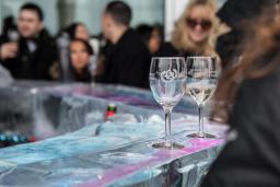 Two wine glasses sitting on a bar top with a crowd of people in the background.