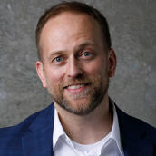 Tyson Lybbert from the shoulders up wearing a white button up shirt and blue suit jacket, no tie