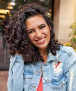 Photo of Jessica Serna, woman wearing a denim jacket with curly brown hair smiling at the camera