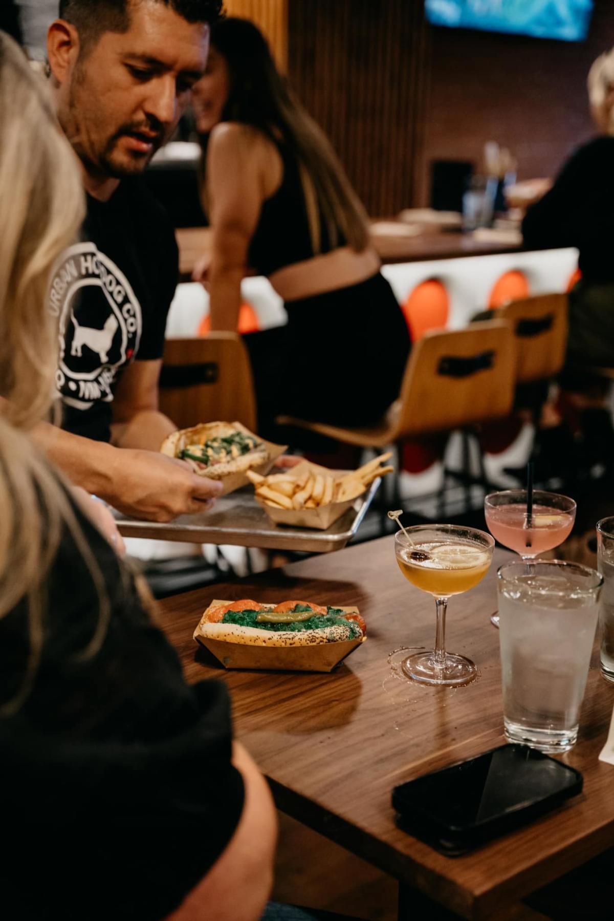 A server at Urban Hotdog Company serves hot dogs to a table.