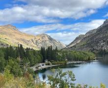 A view from a bit above a lake with mountains, clouds, and trees