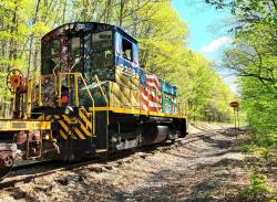 Picture of the North Shore Railroad America 250 PA Train rolling down the tracks through a tree lined rail.
