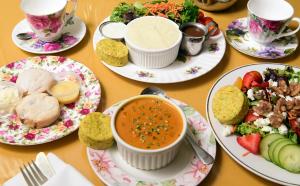 Ornately decorated plates and teacups arranged on a table with selections for brunch at The English Tea Room, including soup, salad, sweet and savory scones and creamy spreads and sauces.
