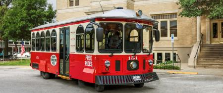 Downtown McKinney Trolley - red and beige - on front of large cream colored building
