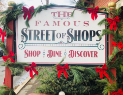 The Street of Shops Road Sign Decorated with Holiday decorations, red bows, and greenery.
