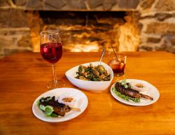 Picture of food on plates with glass of wine and mixed drink on a table by the fireplace at Penn's Tavern
