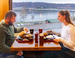Picture of a couple sitting at table by a big window at Skeeter's BBQ with beautiful river valley views just outside. The table is filled with yummy food from the restaurant.