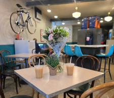 Picture of Cycle Up Cafe & Bike shop cafe room with a table in the forefront that has flowers and ice coffees sitting on it with a bike hanging on the wall in the background