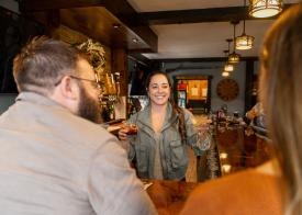 Picture of smiling bar tender delivering drinks to a couple sitting at the bar at Penn's Tavern