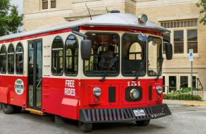 Downtown McKinney Trolley - red and beige - on front of large cream colored building