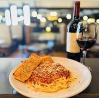 Picture of pasta dish with bread on the side and a bottle of wine with a poured glass beside it at Boondocks Wood Fired Grill